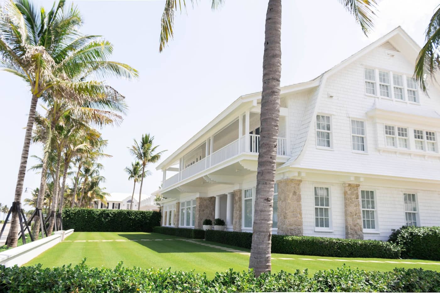 White two-story Florida home under royal palms with a deep green lawn in bright sun