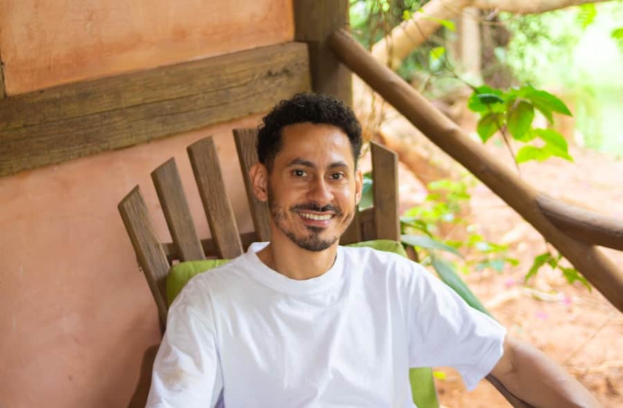 Gus Herrera, founder of Mockingbird Pest Co., smiling in a chair on a sunlit porch surrounded by greenery